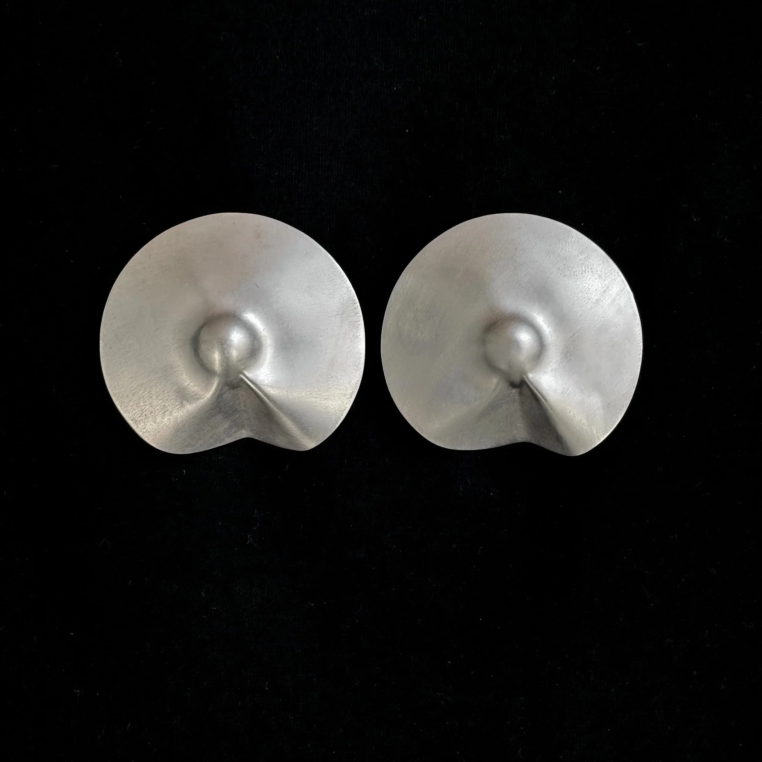 Two silver, round, metallic objects with a concave design on a black background.
