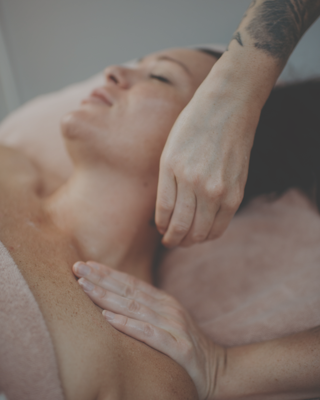 Person receiving a massage with closed eyes, lying on a massage table, with a massage therapist's hand applying pressure to their shoulder.