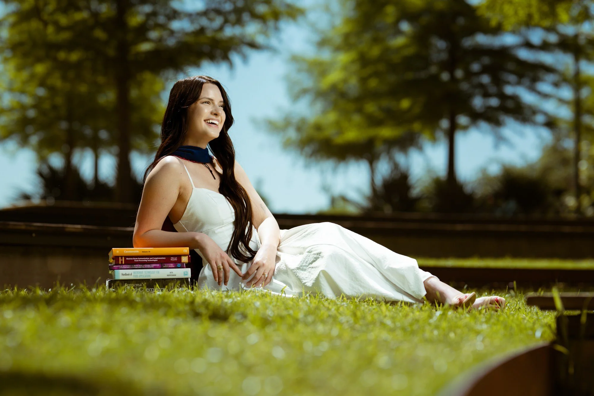  Texas A&amp;M graduation portrait of woman in white dress lying in grass with books, College Station TX 