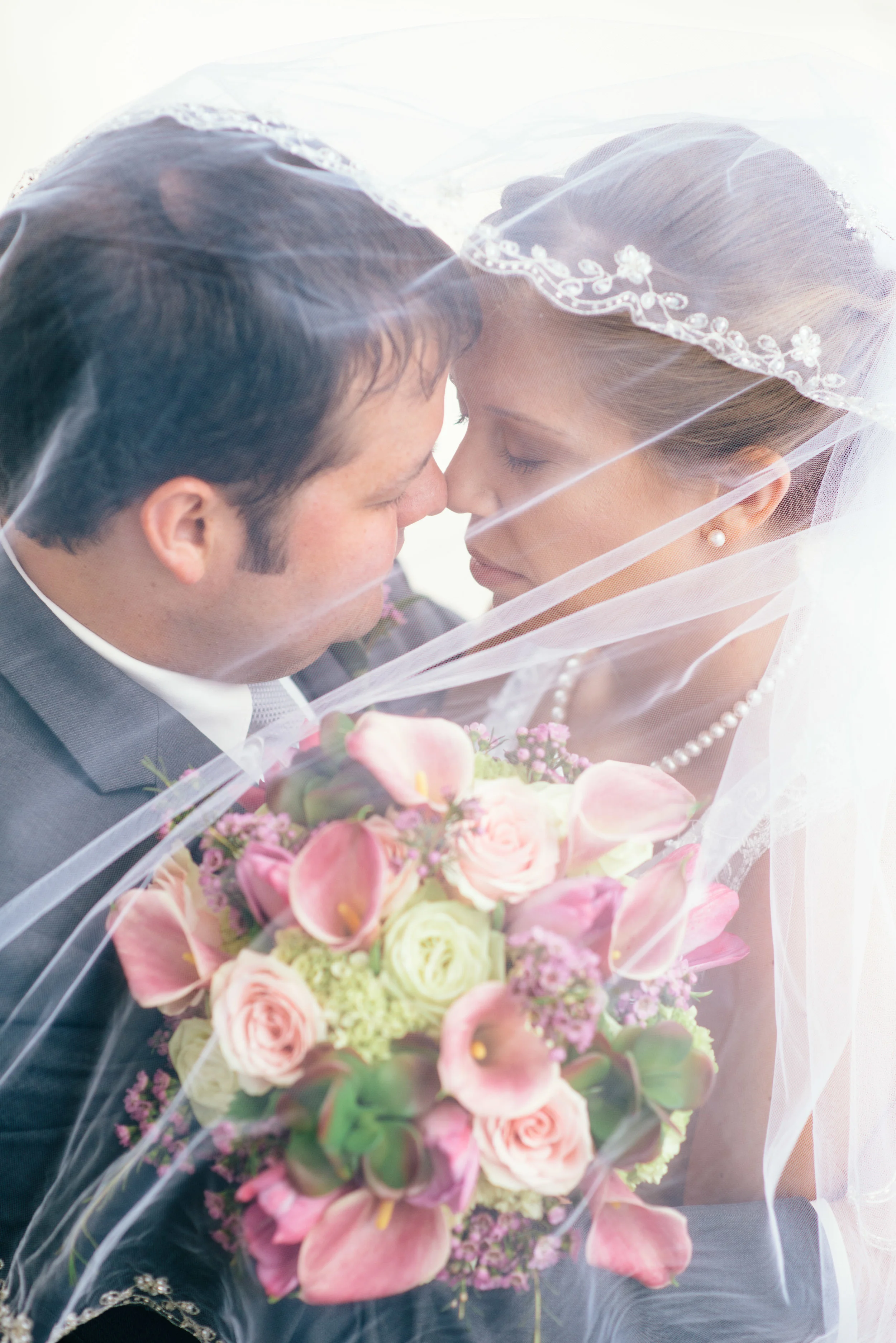 Bride wearing Tiffany's pearls and her groom sharing an intimate moment under a lace veil