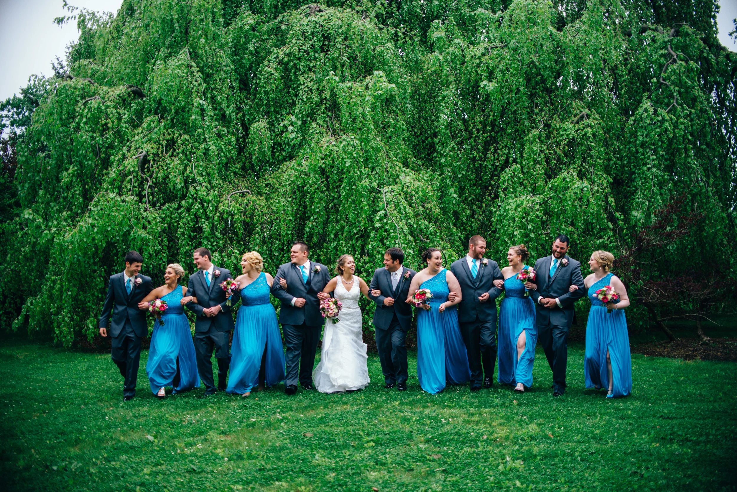 Blue and grey bridal party walking in a garden laughing arm in arm