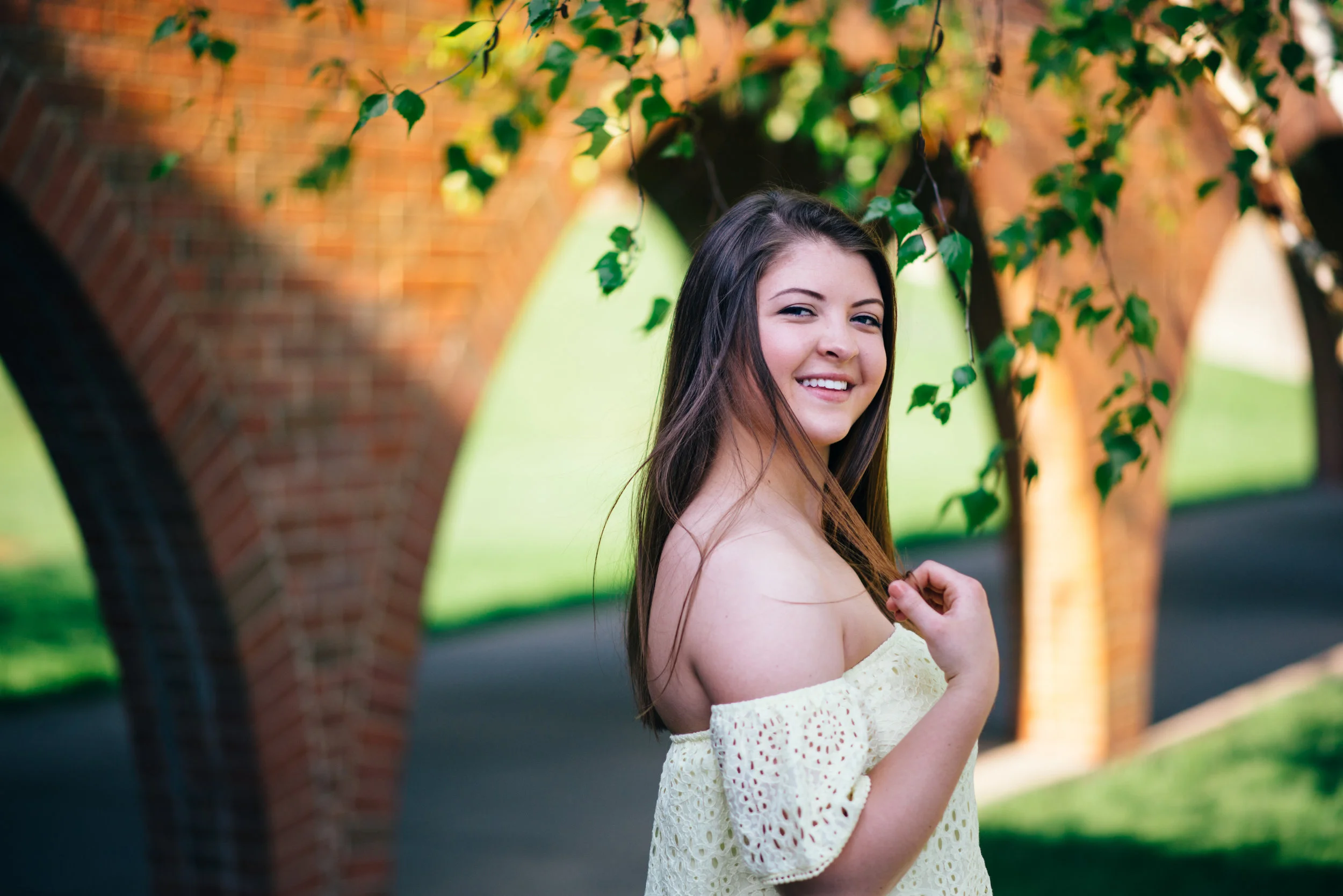 high school senior model with off the shoulder yellow lace top posing in front of arches at the Indiana University of Pennsylvania