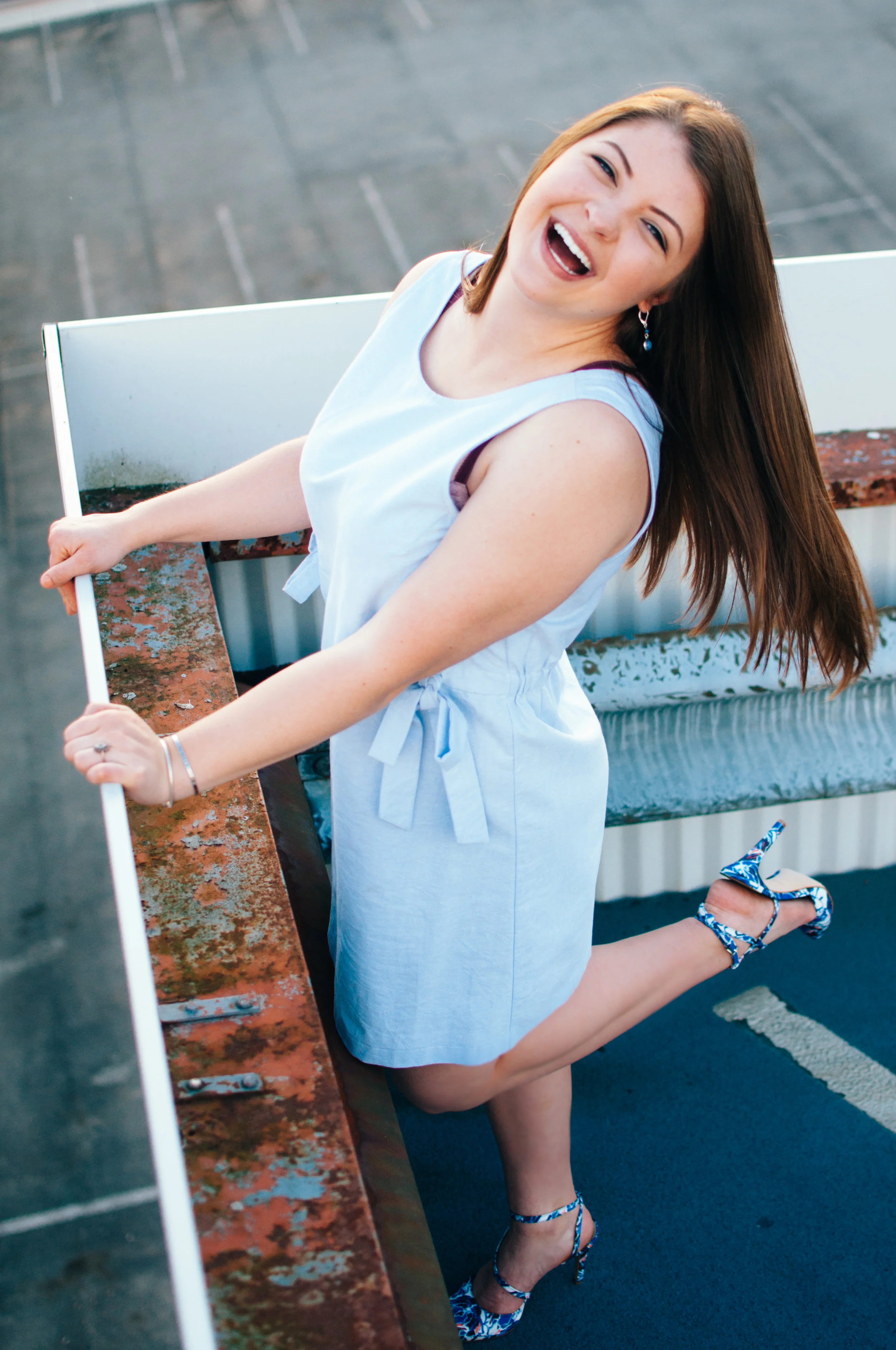 top down shot of high school senior model laughing in light blue shift dress standing on top of parking garage overlooking city of Indiana PA