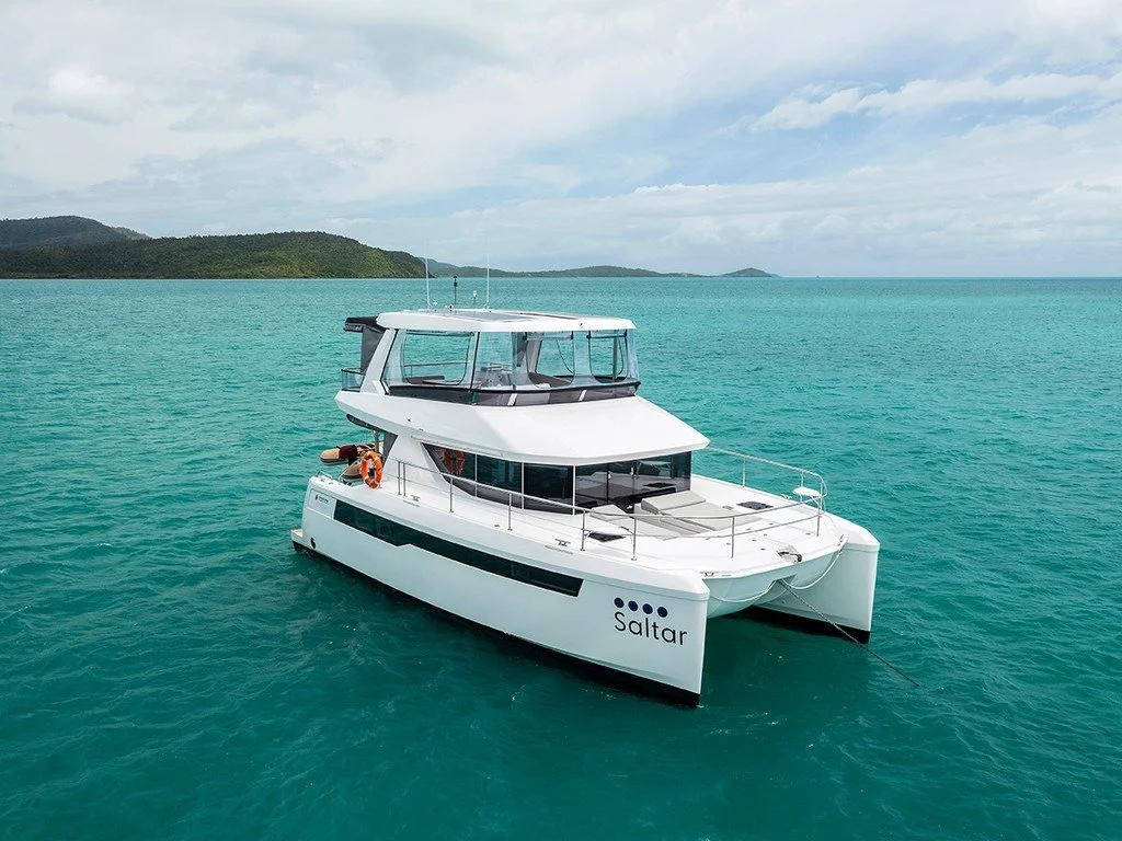 A white yacht named 'Saltar' floating on clear turquoise water near an island with green hills.
