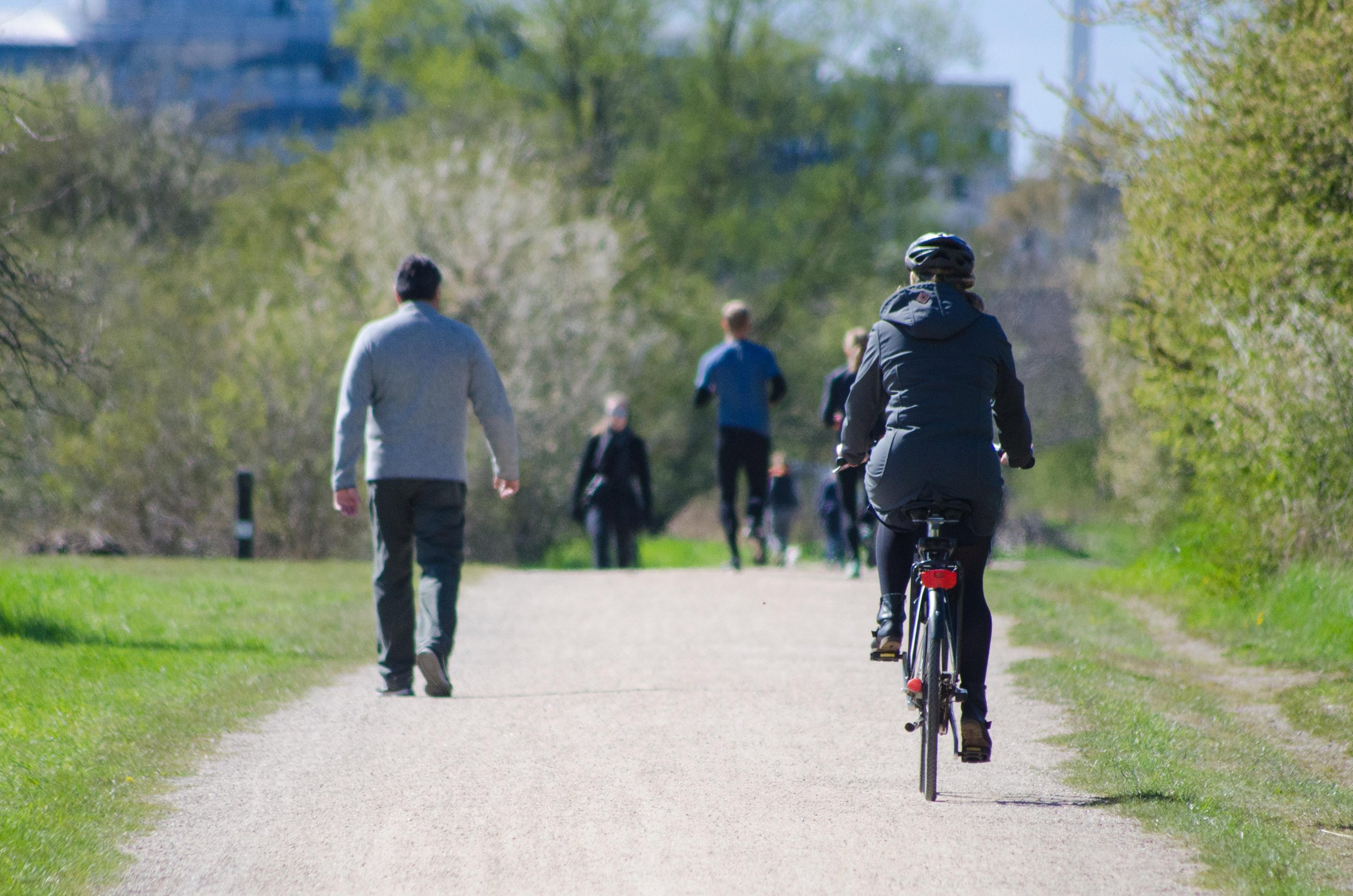 Walkers, joggers, and bikers enjoy a park trail with skyscrapers in the background
