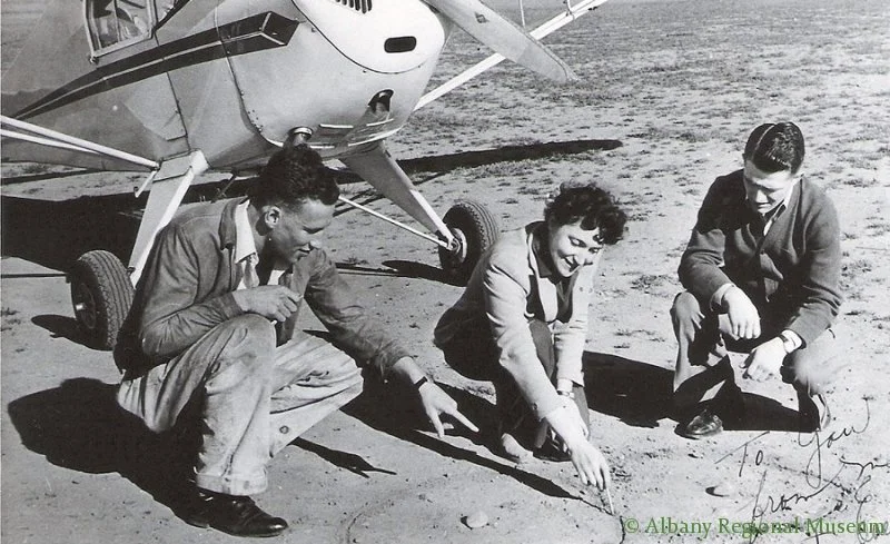 Evelyn Burleson maps strategy in sand with two aviation students at the Albany airport.