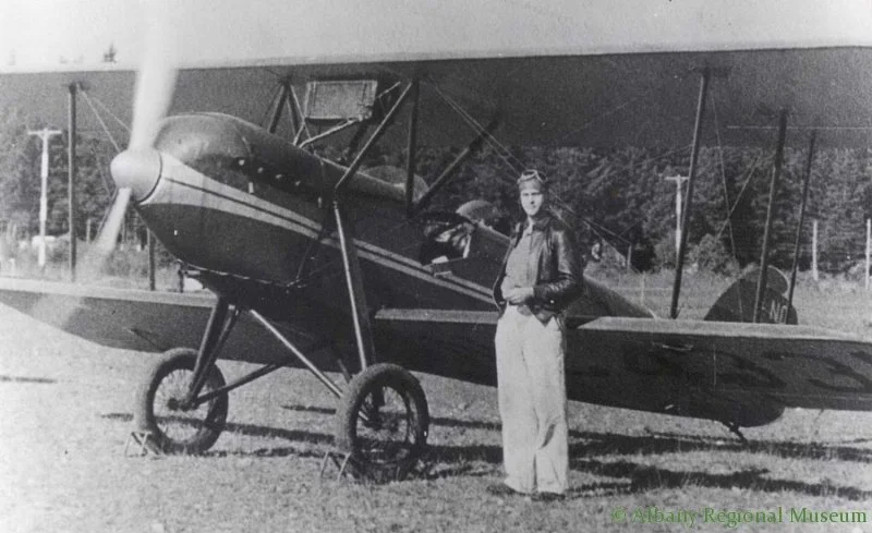 Photo of George Douglas standing in font of his plane, a Waco 10-0x5 single engine, at Albany Airport, 1929. George Douglas (born 1911), one of the early mangers of Albany Airport (Langmack Field) in the 1930s.