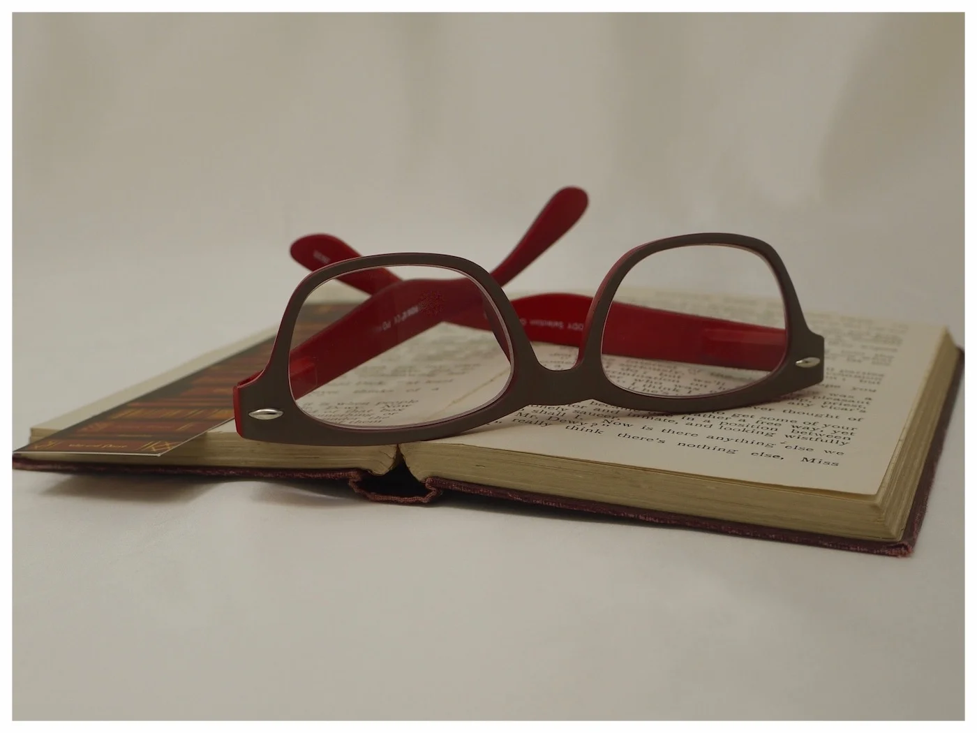 grey and red contemporary reading glasses placed upside down on an open book