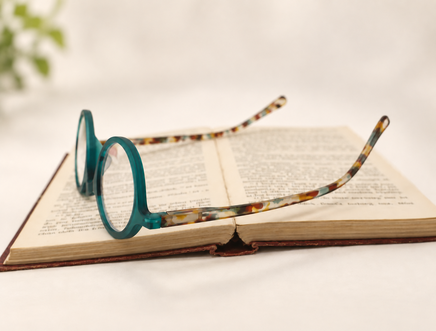 Three-quarter view of Ikaly Lisboa blue light reading glasses with a round teal front and patterned temples