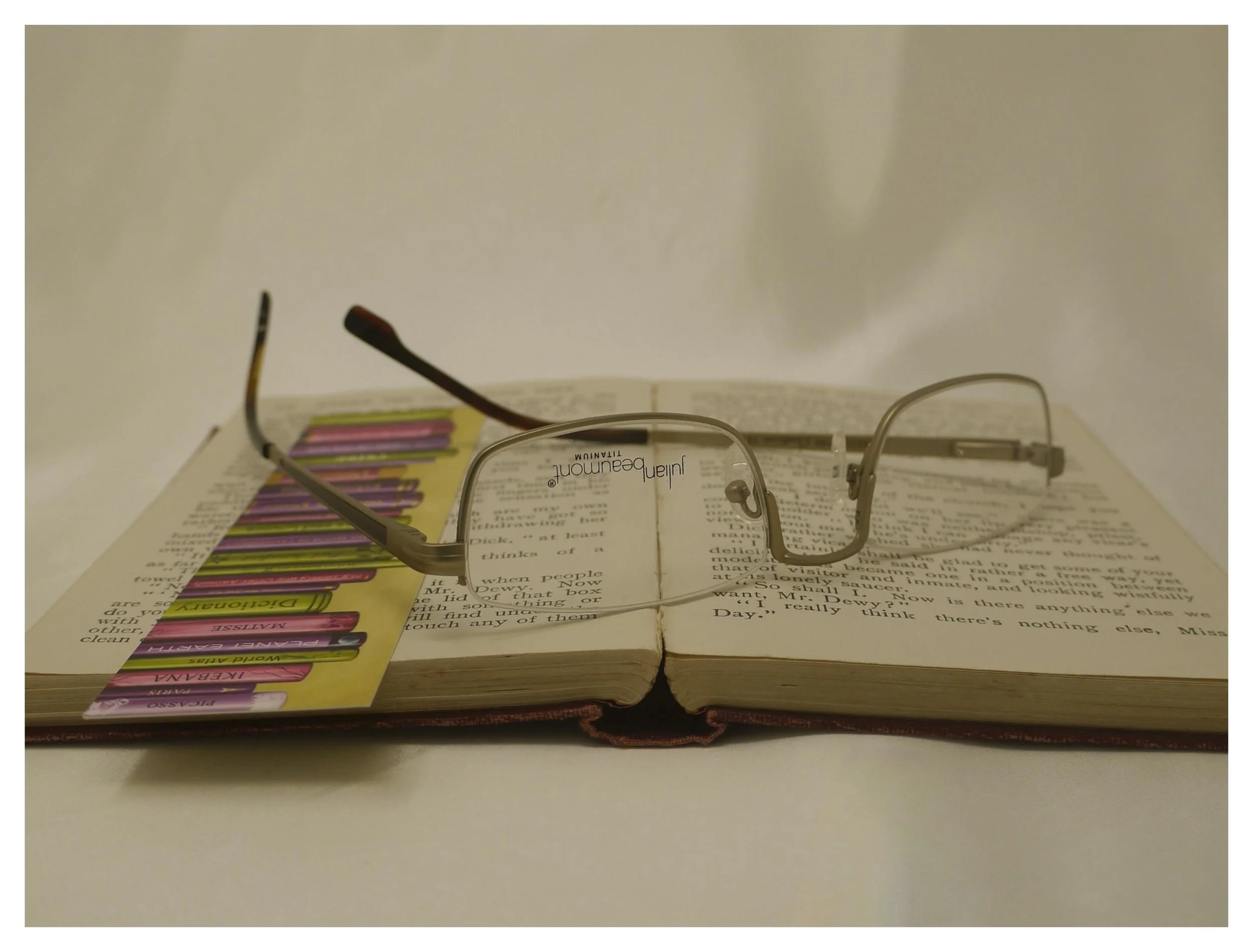Rear-angle inverted view of Julian Beaumont 3659 gold titanium half-eye reading glasses on a book, showing hinge and temple detail