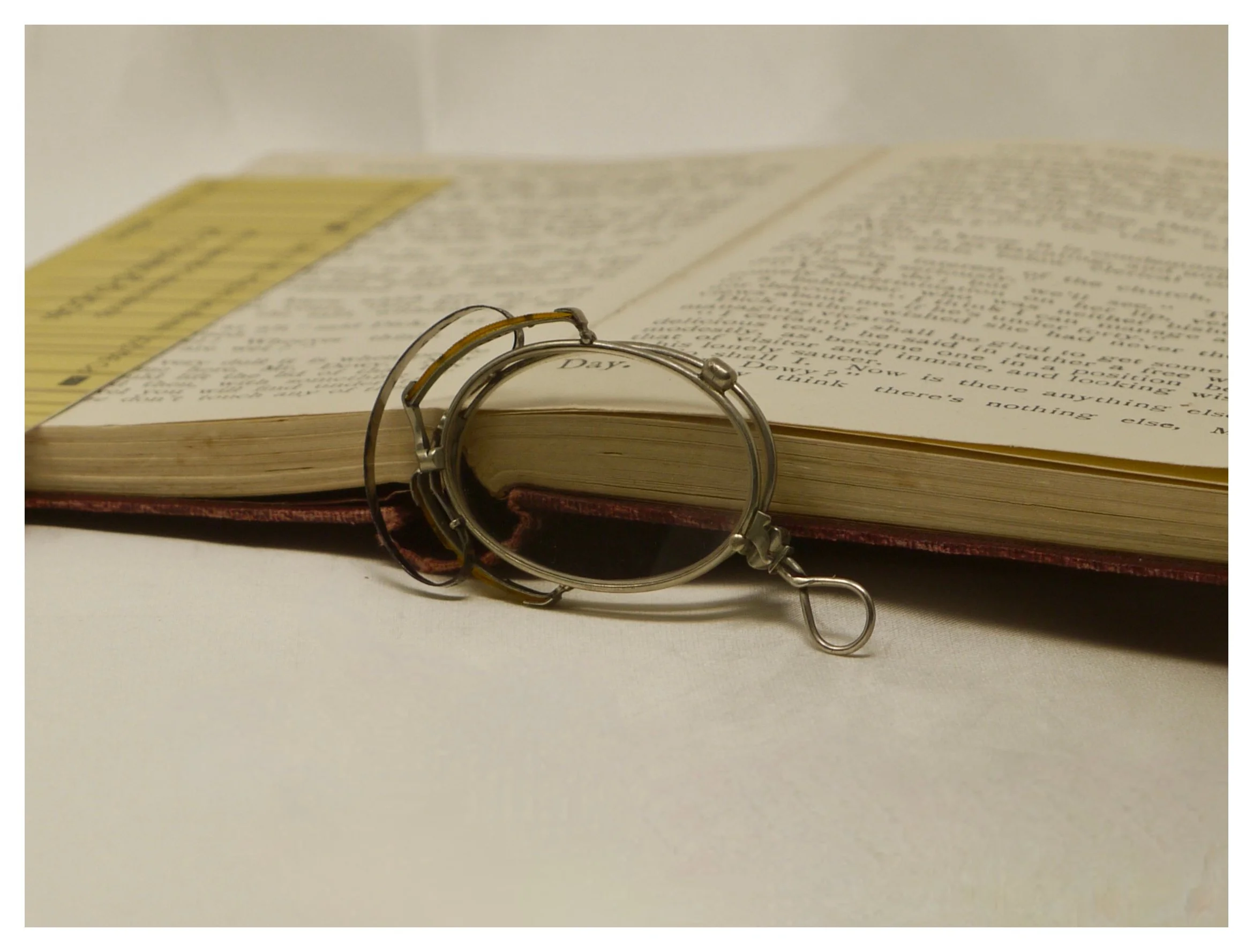 Side view of antique silver pince-nez folded using the hook-and-pin mechanism, resting on a book.
