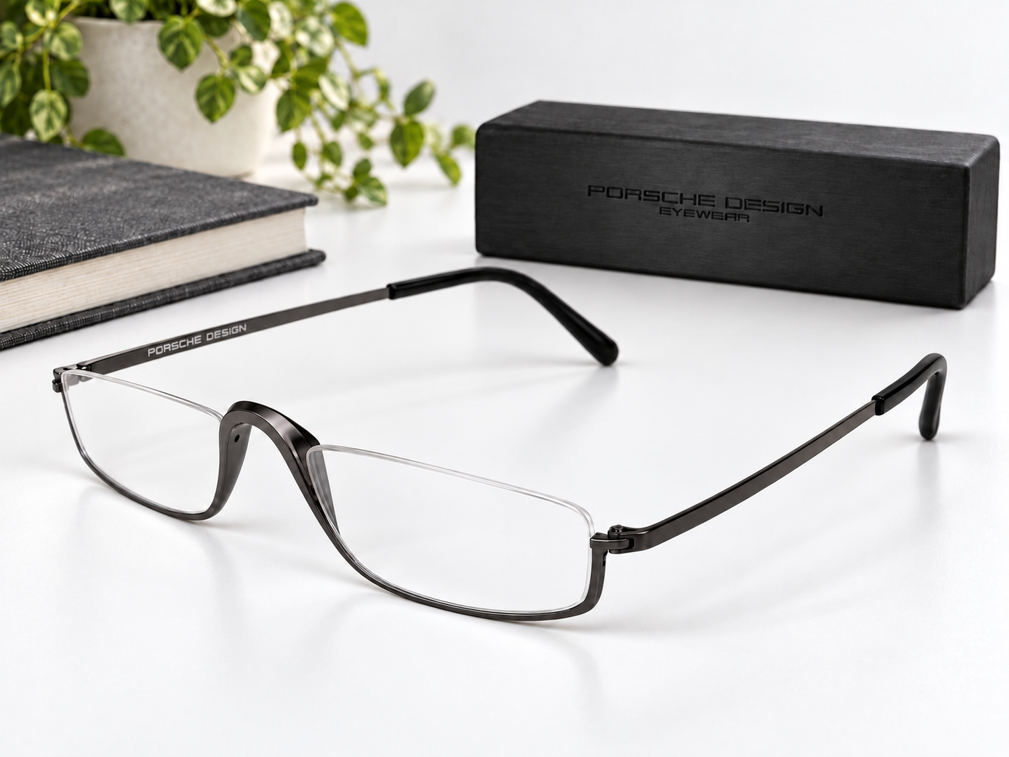 Porsche Design P8002-C reading glasses beside a black Porsche Design case, book and plant