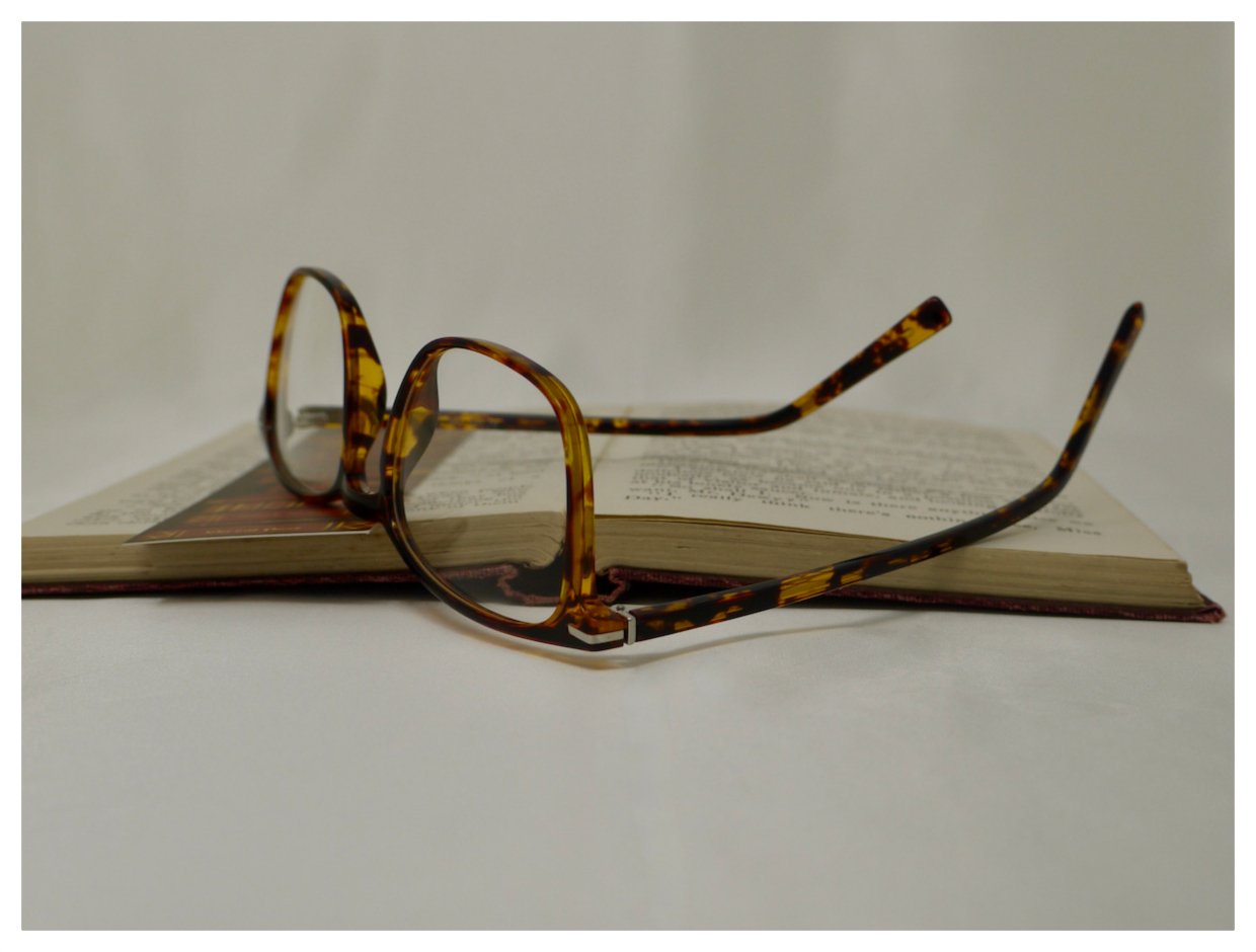 Folded tortoiseshell spectacles resting on book pages showing the rich acetate finish