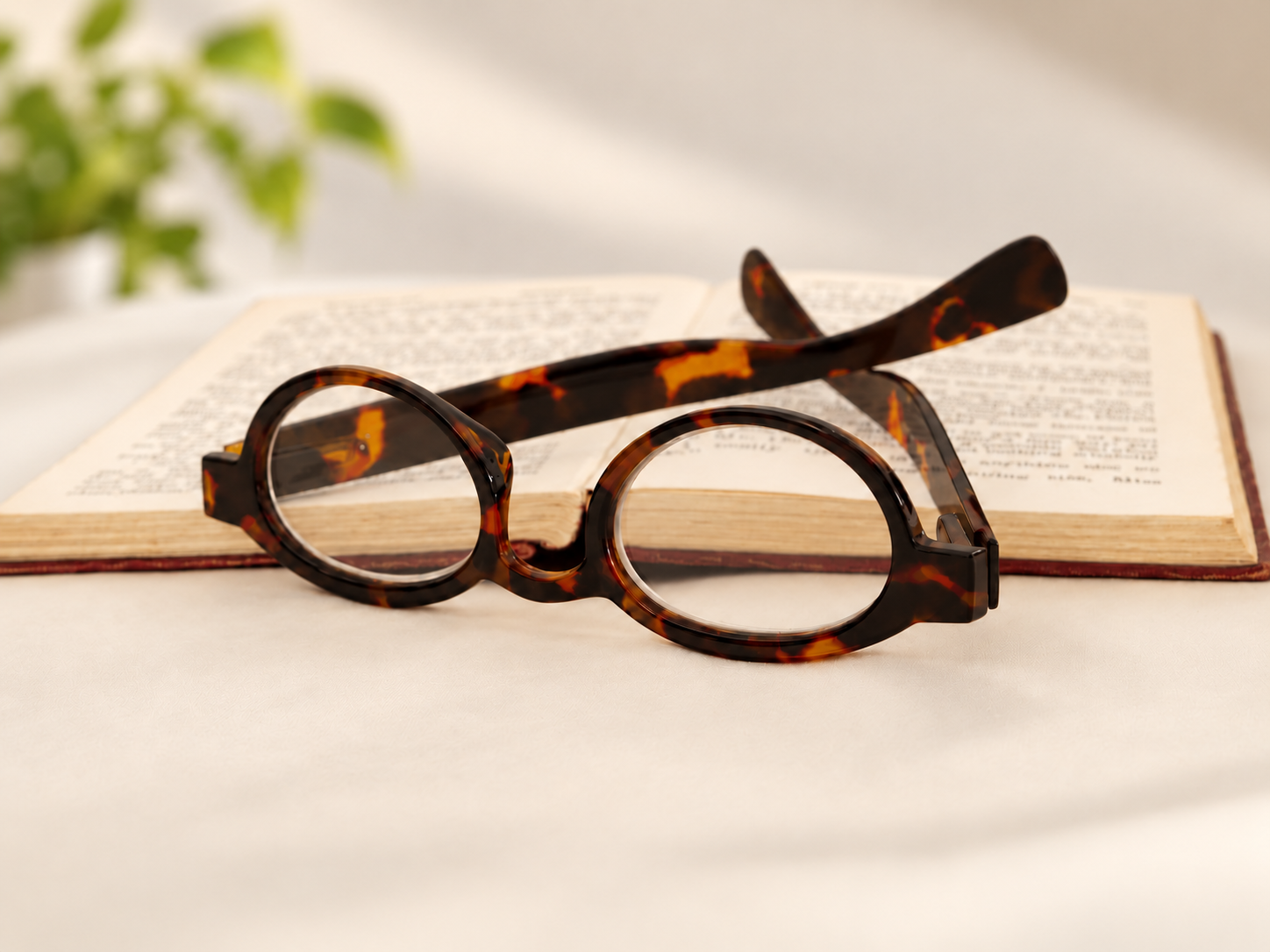 L40 oval tortoiseshell reading glasses positioned in front of an open book