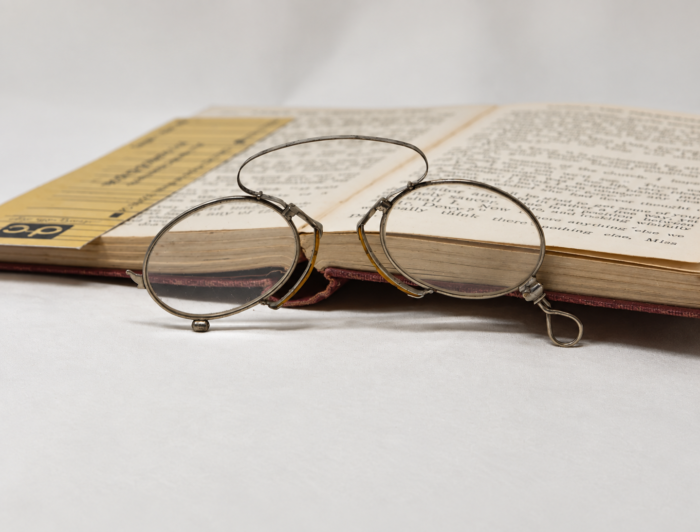 Antique silver-tone pince-nez folded beside an open book, with its loop handle visible