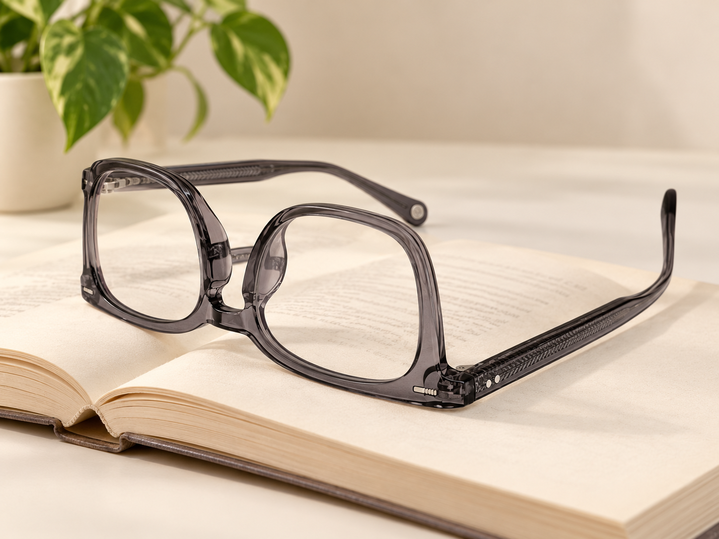 Jacob Stone JS811 grey reading glasses resting upside down on an open book beside a green plant