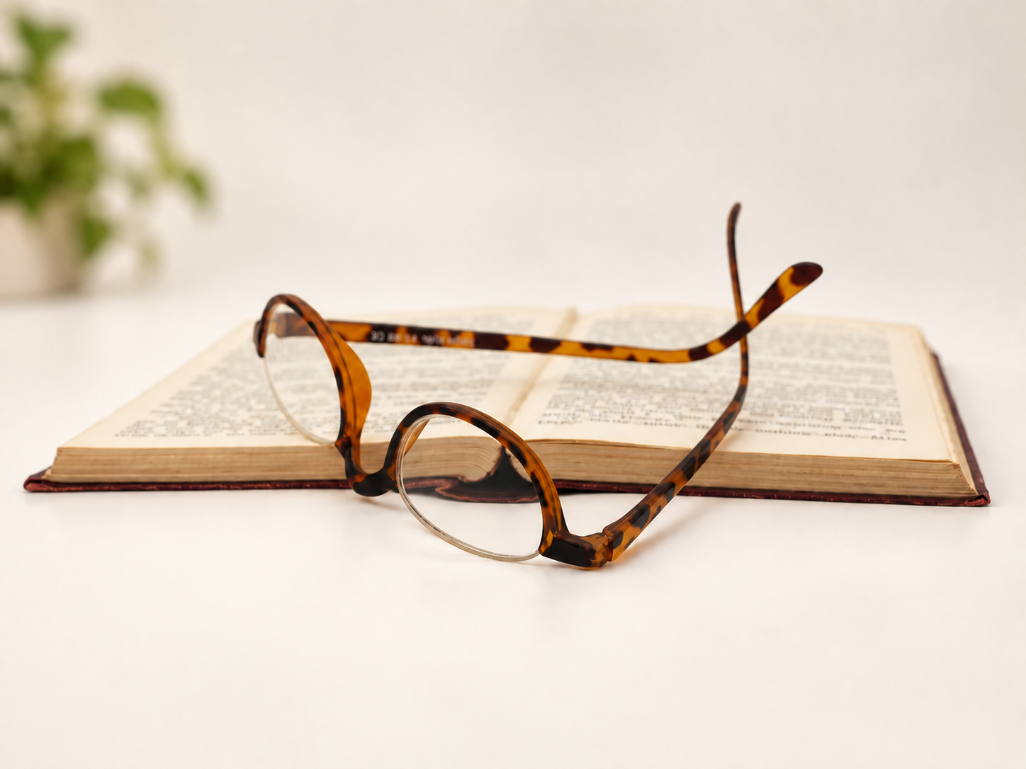 Vermont tortoiseshell semi-rimless half-eye reading glasses resting upside down on an open book