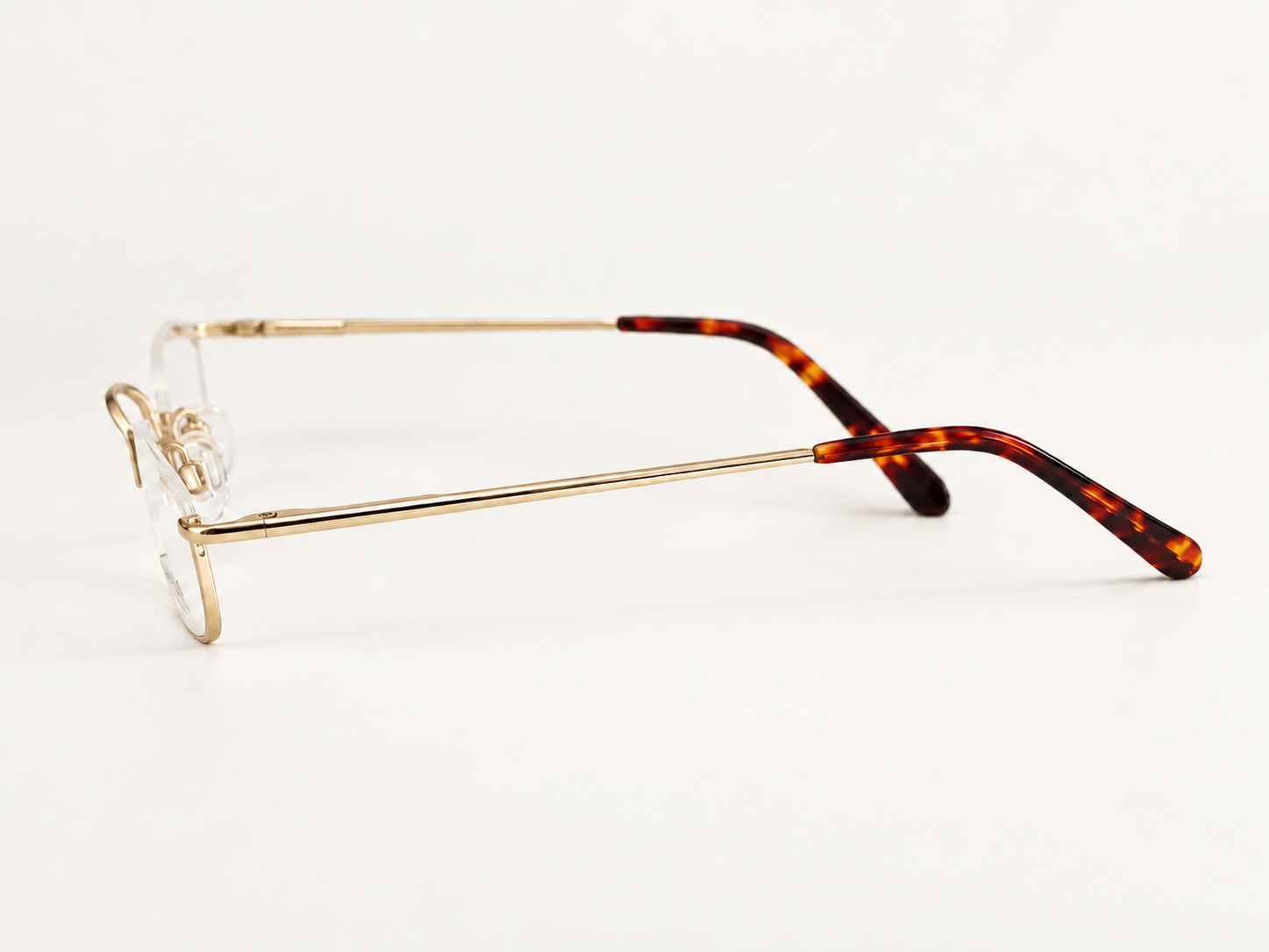 B-AQ gold half-eye reading glasses resting on an open book, with softly blurred green leaves in the background