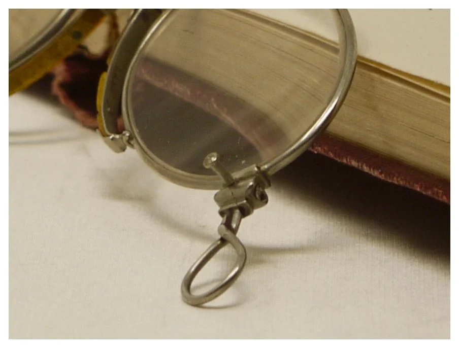 Close-up detail of the loop handle and hinge mechanism on antique silver pince-nez eyeglasses.