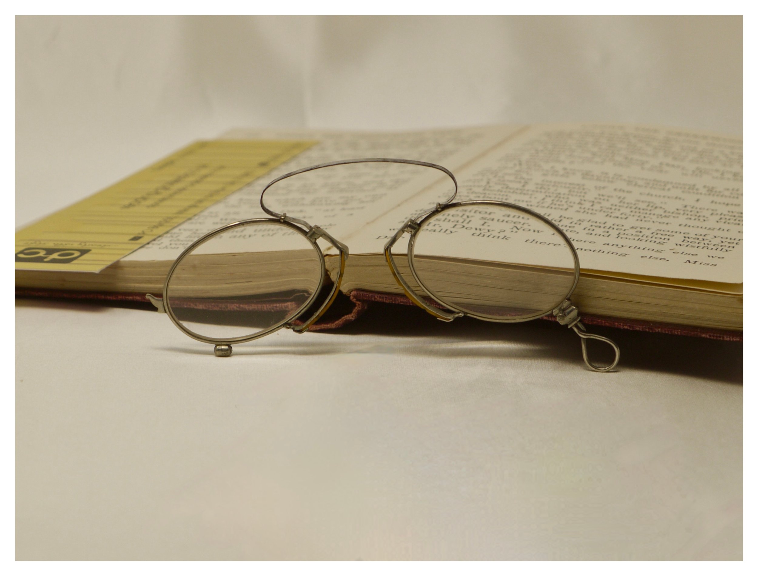 Antique silver folding pince-nez eyeglasses open and resting upright on the pages of an old book.