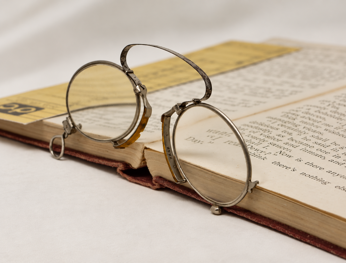 Antique silver-tone folding pince-nez open on a book, showing both lenses and the loop handle
