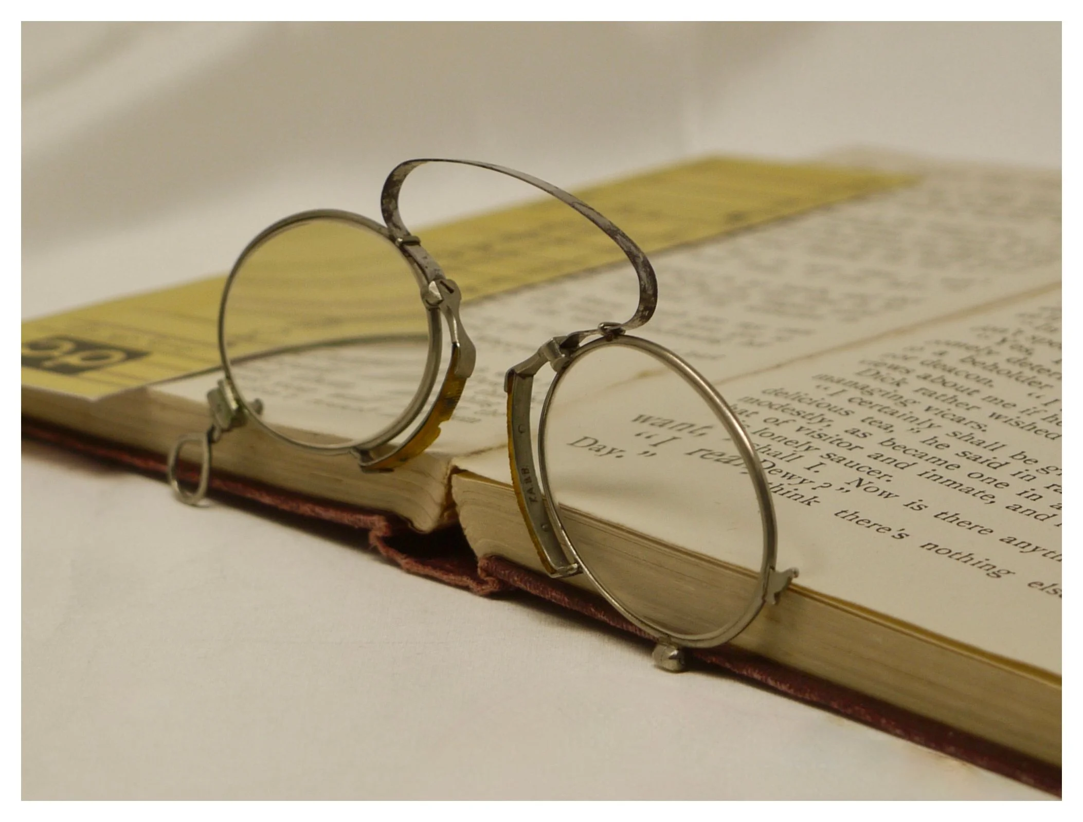 High angle view of vintage silver pince-nez glasses open on a book, highlighting the curved bridge spring.