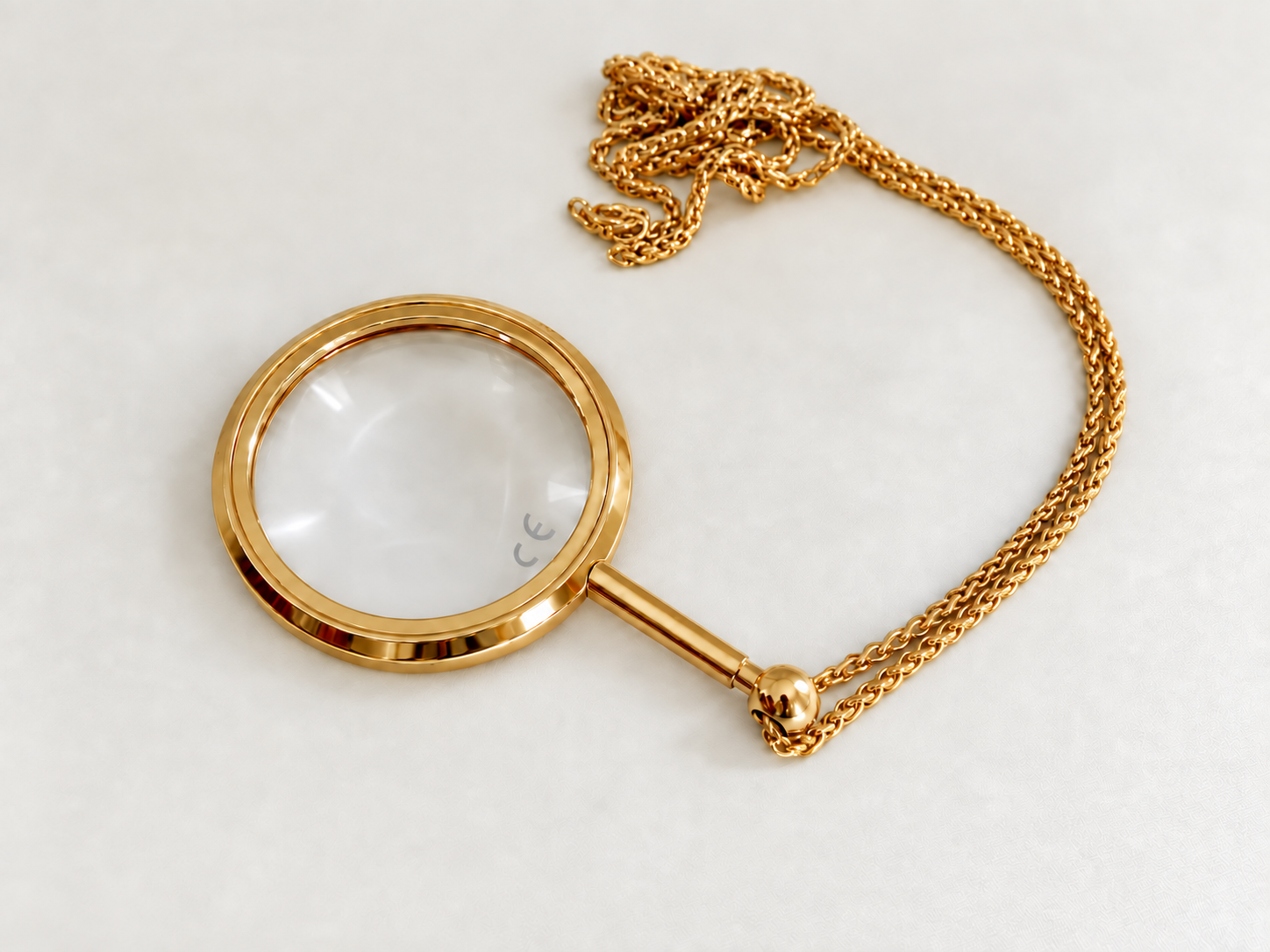 Eschenbach gold pendant magnifier with a round glass lens and matching chain on a pale background