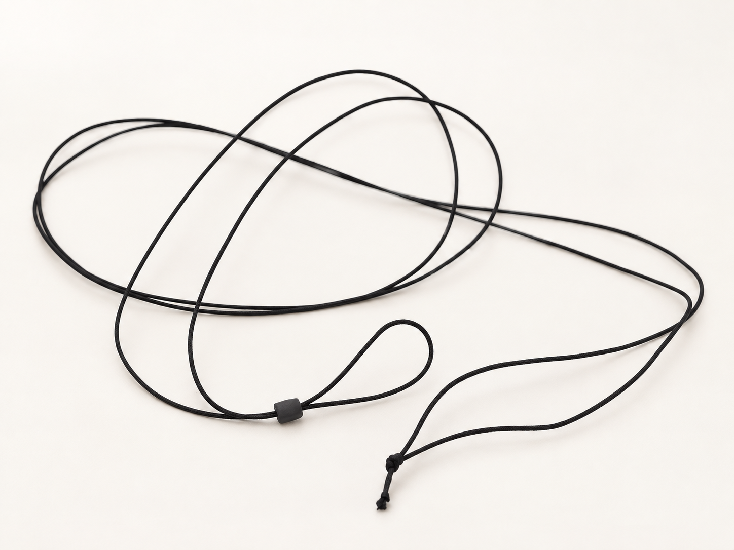 Fine black monocle cord laid in loose loops, showing its small sliding piece and knotted end