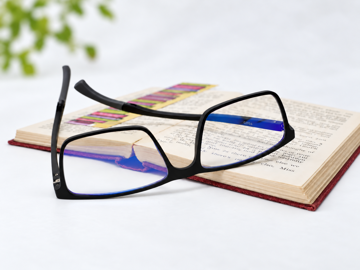 C-2926 reading glasses resting beside an open book, with blue reflections on the clear lenses