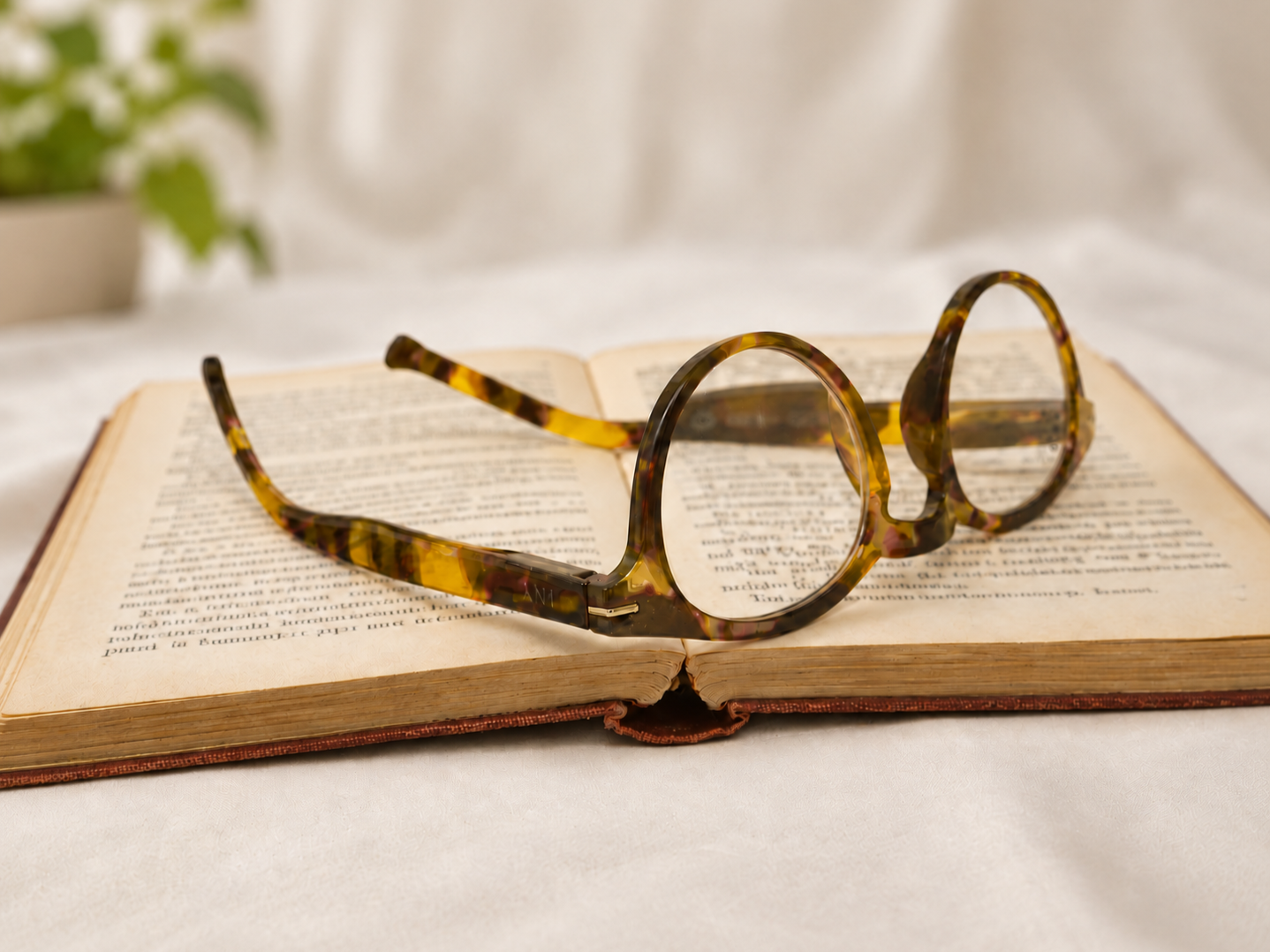 Frankie light tortoiseshell Panto reading glasses resting upside down on an open book