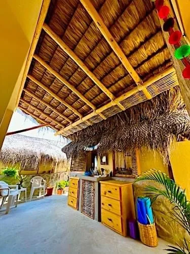 Outdoor restaurant or bar with thatched roof, yellow walls, and tropical decor, including potted plants, colorful lanterns, and outdoor seating.