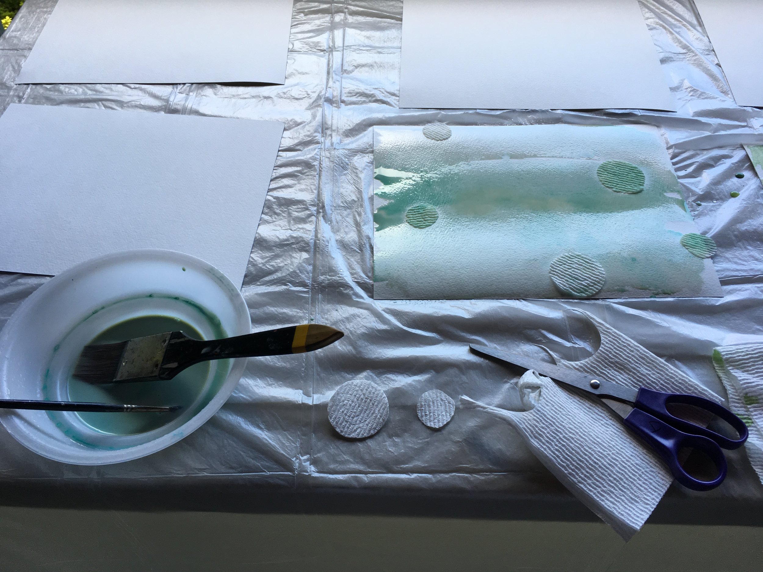 Another process of using paper to create circles in paint. Round paper towel pieces draw water underneath…