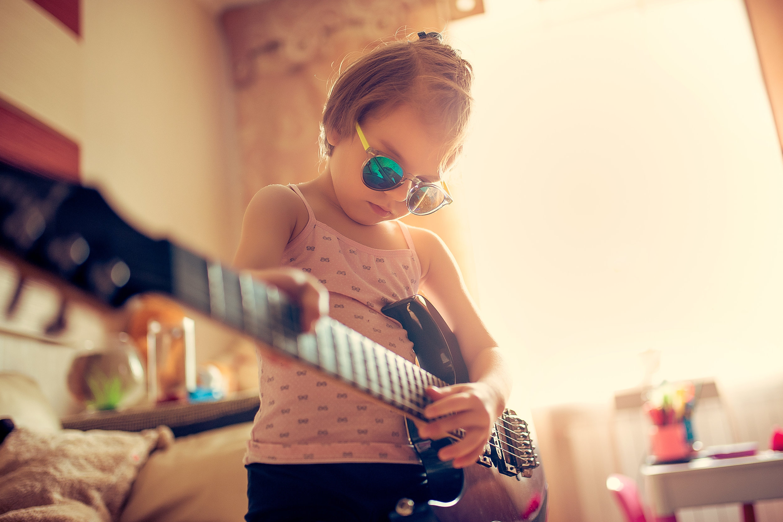 Cute little child girl in sunglasses playing guitar at home
