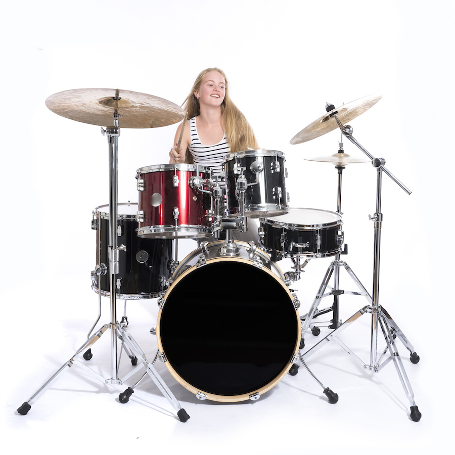 young blond teenage girl plays the drums in studio against white background