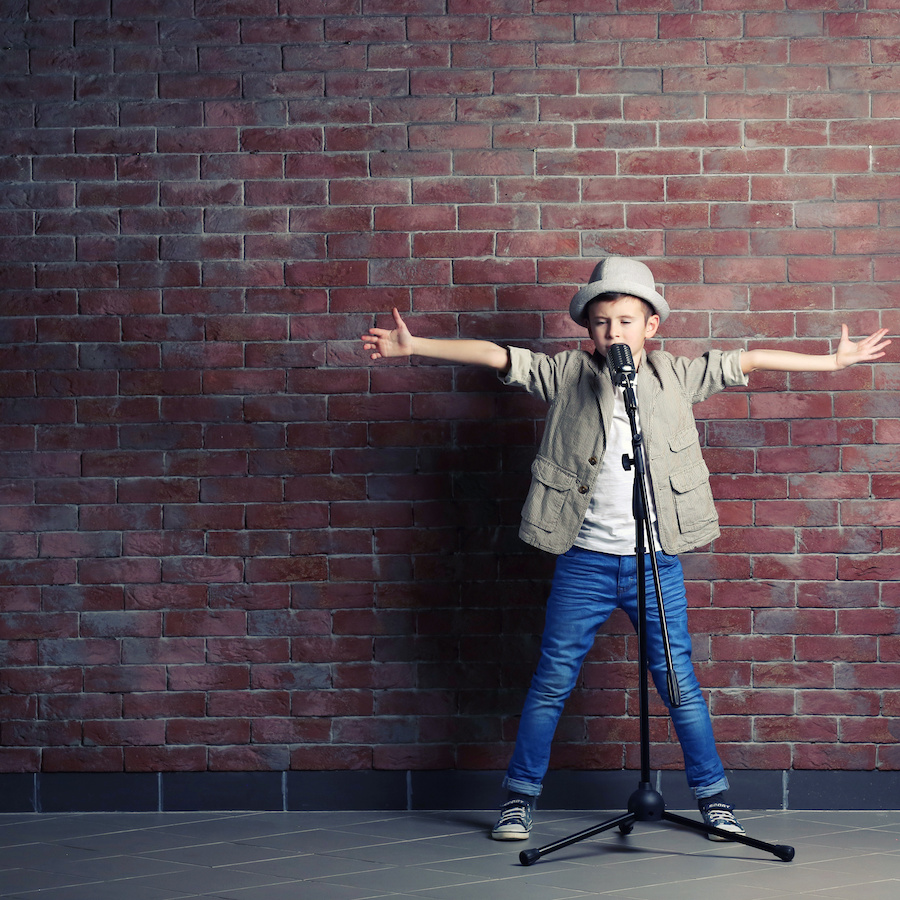 Little boy singing with microphone on a brick wall background