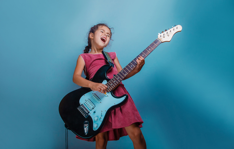 Girl European appearance ten years playing guitar on a blue bac