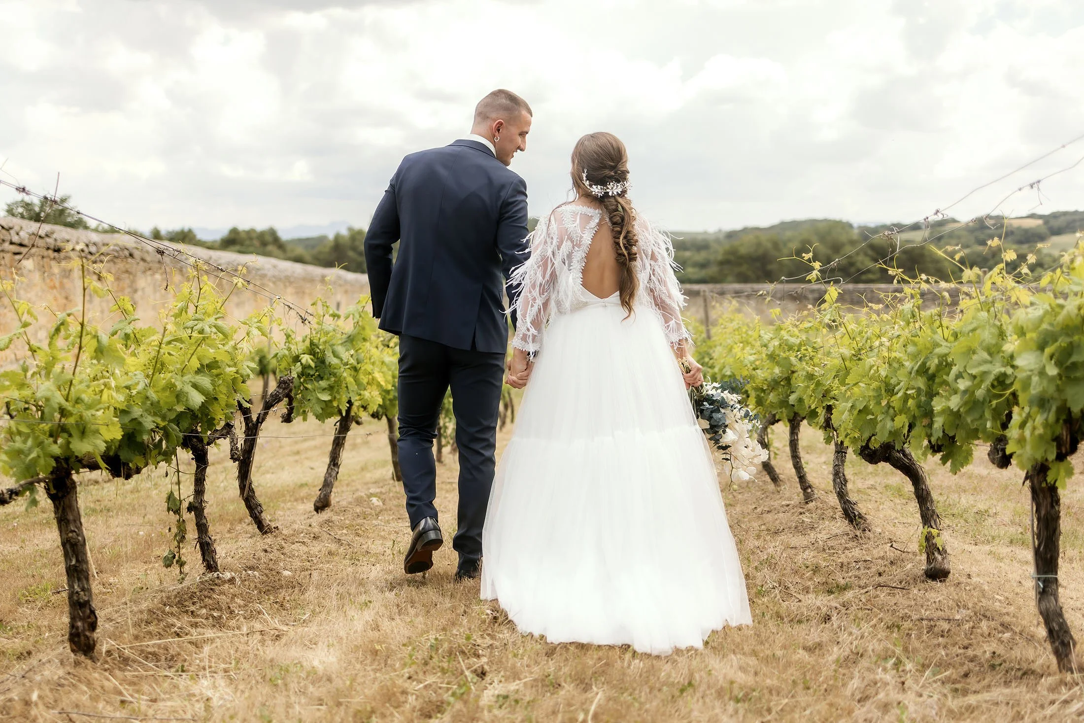 Pareja de novios de espaldas andando sobre los viñedos del Monasterio del Espino
