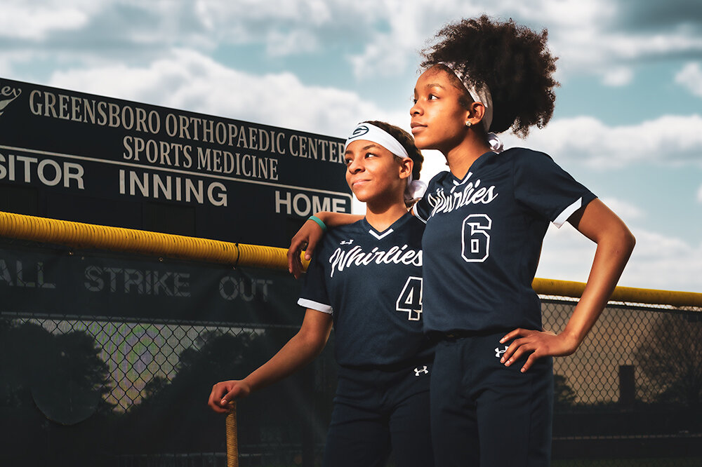 two sisters who play softball together pause in family reflection in the outfield while in uniform in front of the scoreboard by Don Evans Photography in Greensboro NC.jpg