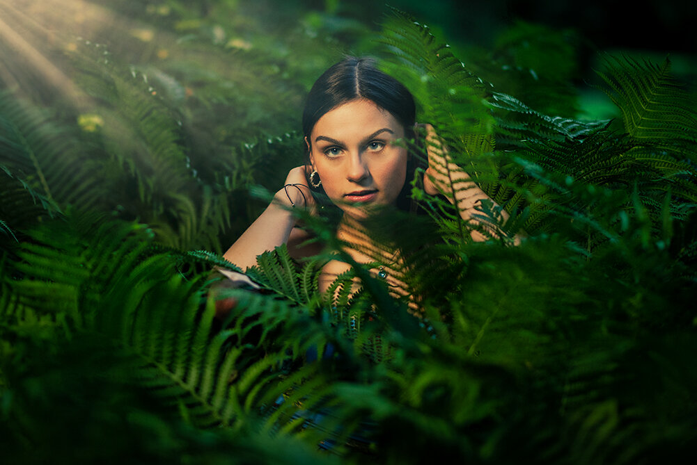 high school senior with dark hair lays down in a bed of ferns and peeks her head up while posing for her senior pictures with Don Evans Photography in Greensboro NC.jpg