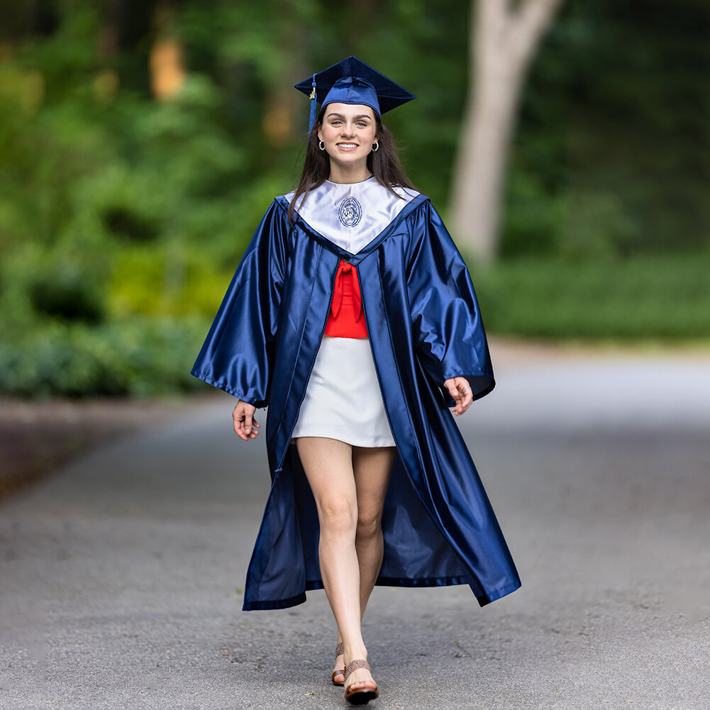 high school senior wearing blue cap and gown and red and white outfit walks down a path in a park during her senior pictures photo session with Don Evans Photography in Greensboro NC.jpg