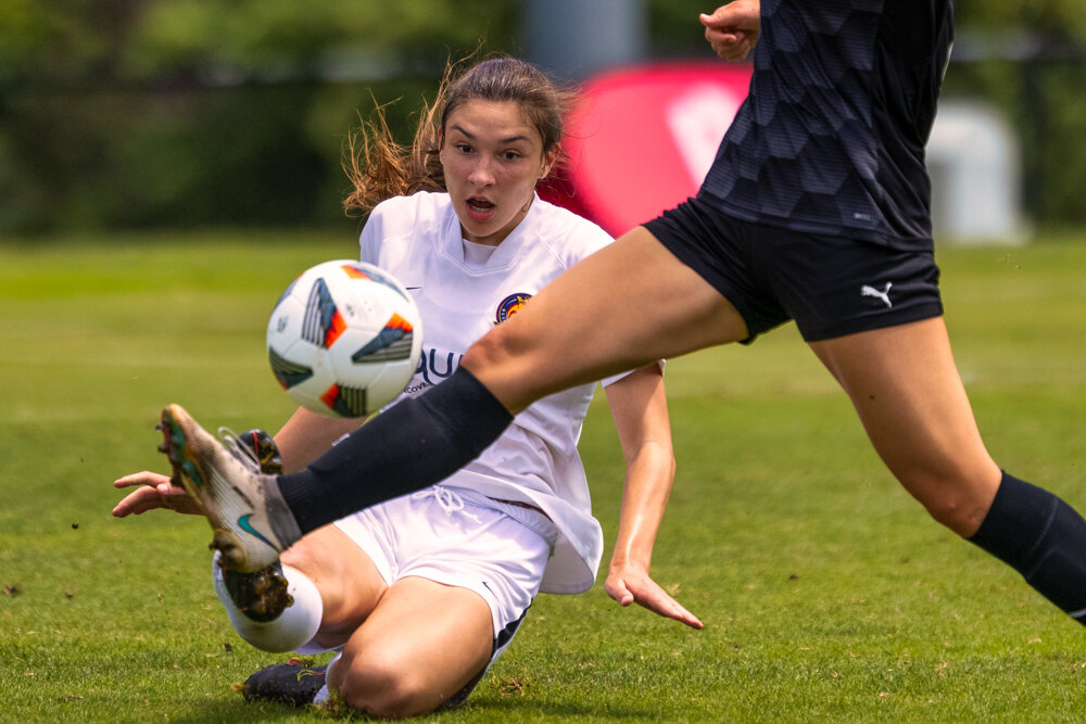  girls academy league soccer player in white uniform slides on the ground and watches as the ball is struck by an opponent during a national tournament taken by Don Evans Photography in Greensboro NC 