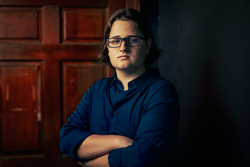 high school senior wearing a blue collared shirt and glasses stands in a doorway posing for his senior picture with Don Evans Photography in Greensboro NC.jpg