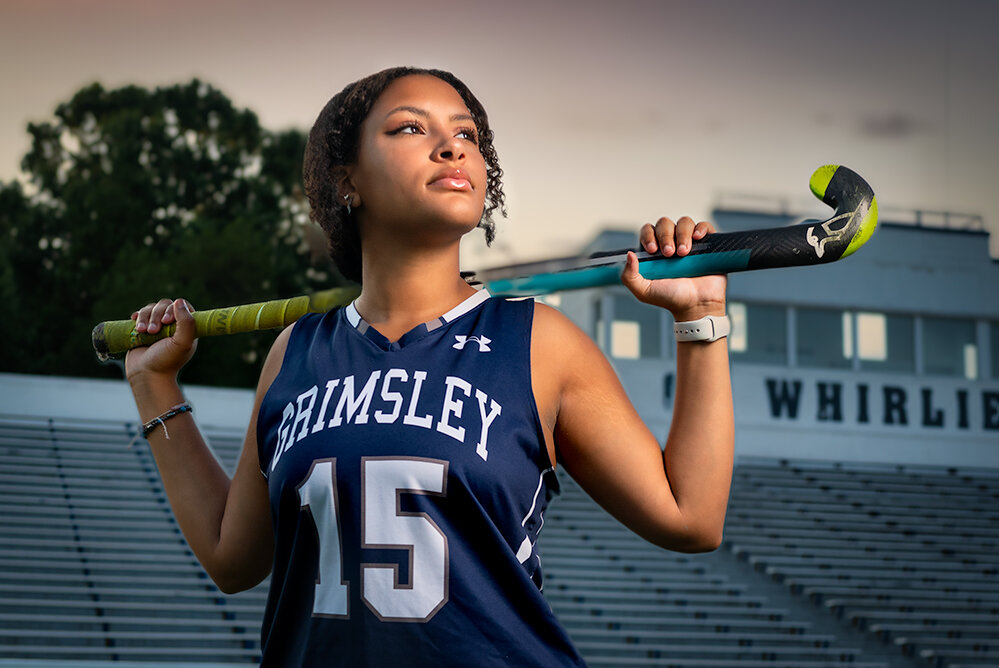 high school field hockey senior in blue uniform stares into the distance in a stadium field at sunset during her senior sports pictures with Don Evans Photography in Greensboro NC.jpg