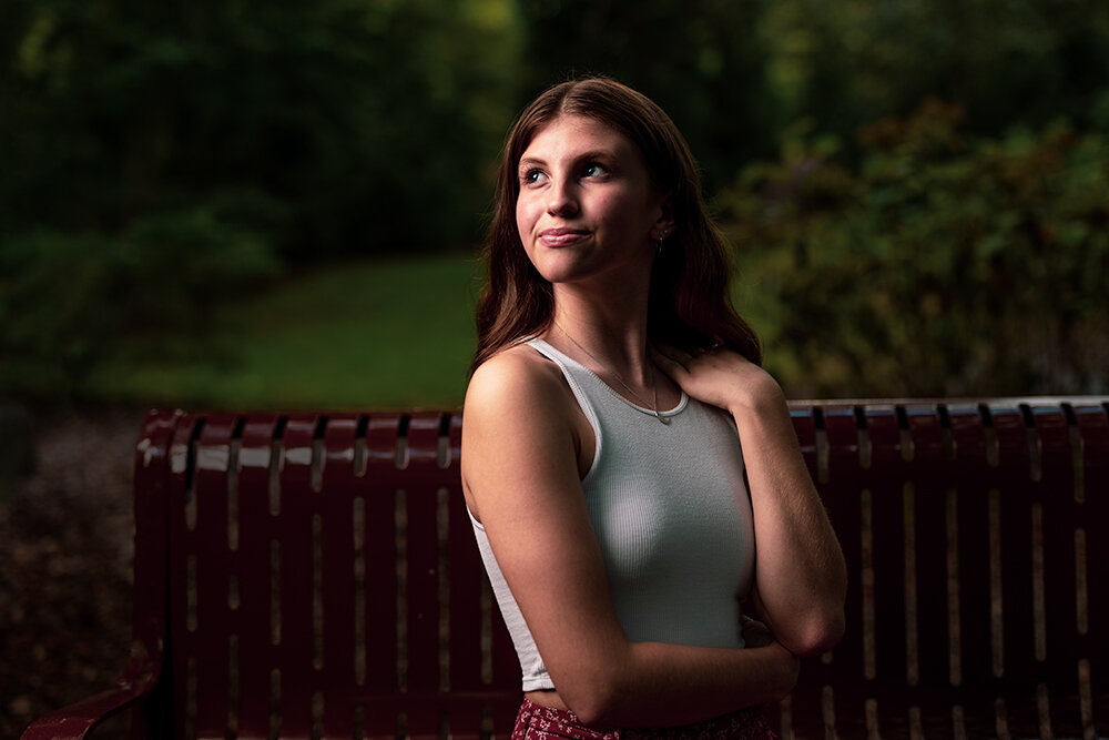 college senior graduate sits on a bench in a park and looks toward the light during her senior picture photo session with Don Evans Photography in Greensboro NC.jpg