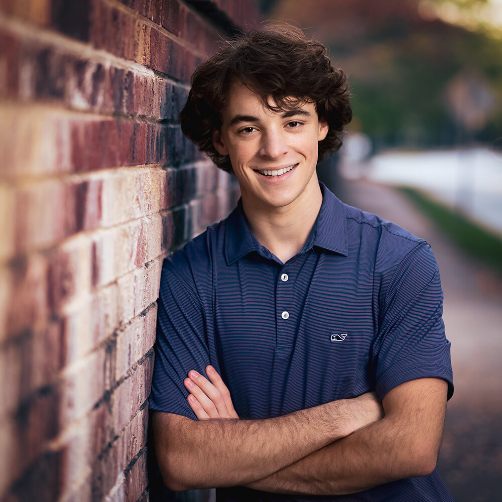 Don Evans Photography in Greensboro high school senior wearing a polo shirt leans against a brick wall during his senior picture photo session.jpg
