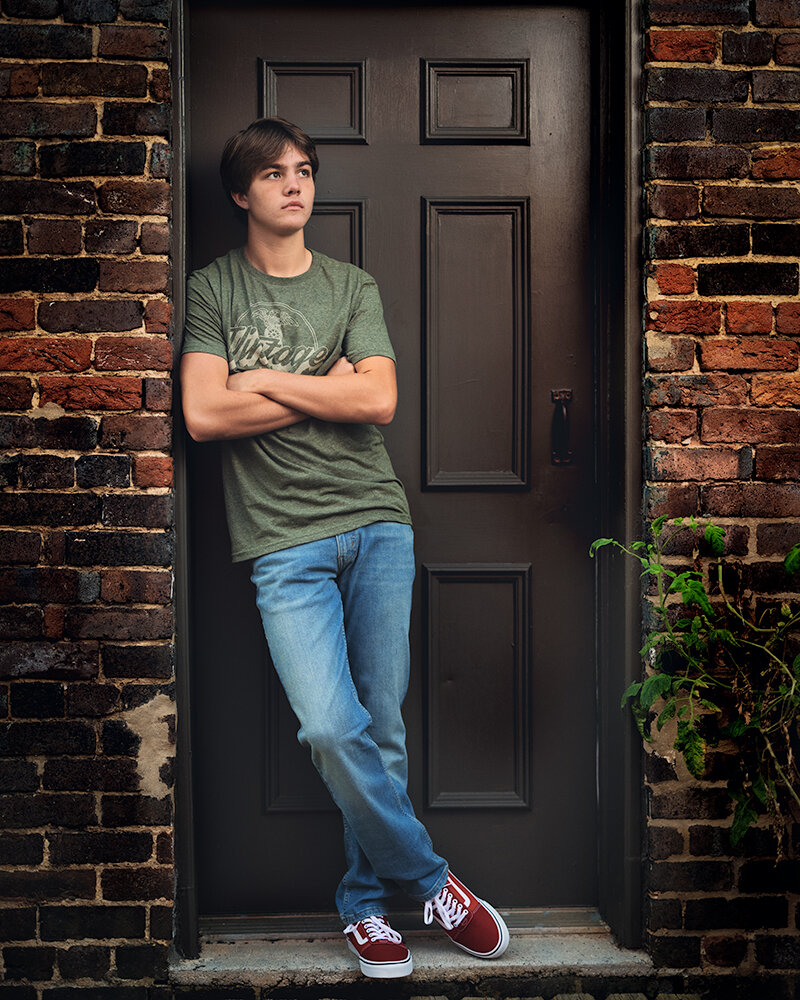  Don Evans Photography in Greensboro high school senior leans against a door during sunrise while having his senior picture photo session 
