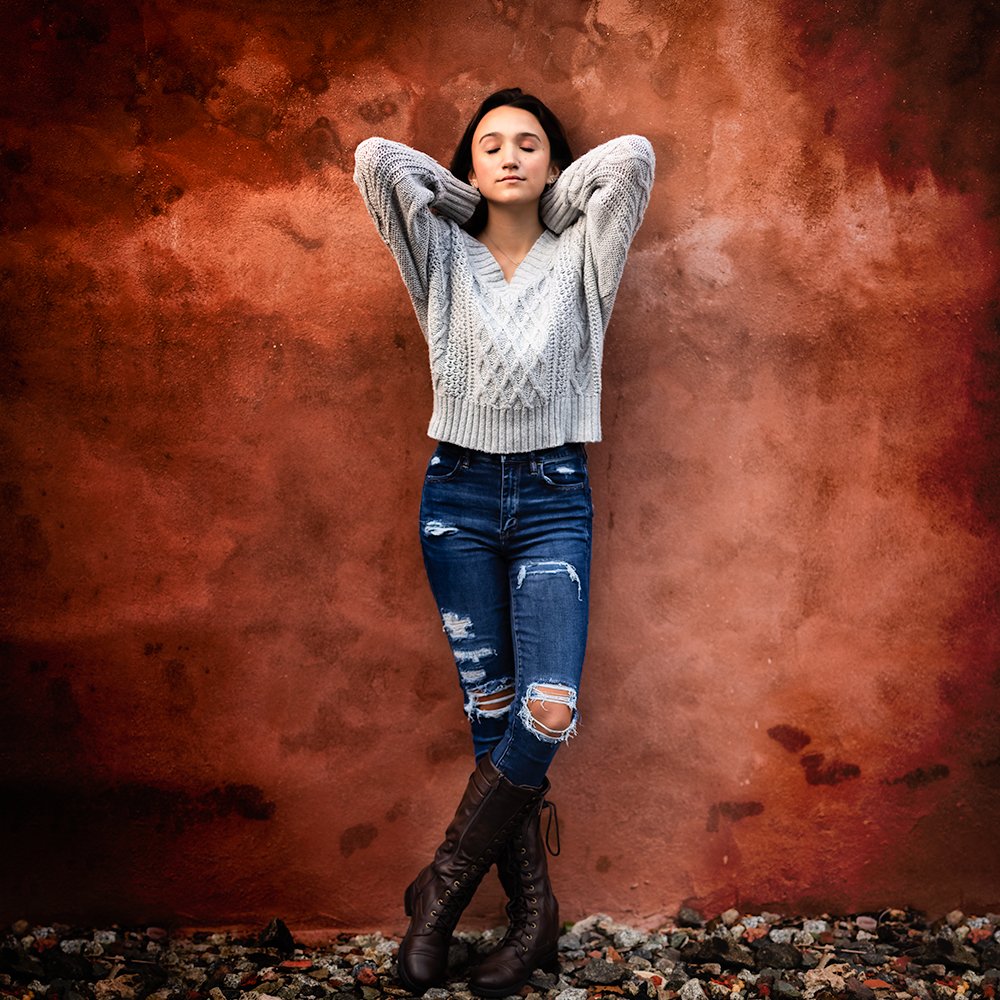 Don Evans Photography in Greensboro high school senior leans against a red wall wearing jeans an top while posing for her senior pictures photo session.jpg