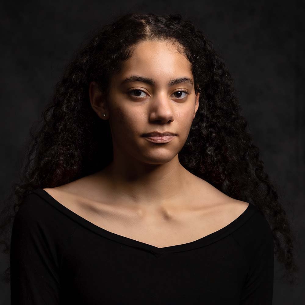 Don Evans Photography in Greensboro college senior wearing a black top sits and looks at the camera while posing for her senior picture photo session in studio.jpg