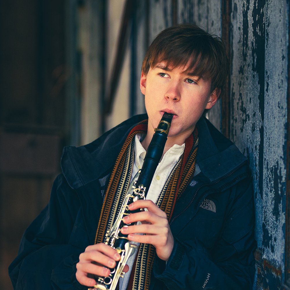Don Evans Photography in Greensboro high school senior clarinettist leans against a wall and plays his instrument during his senior picture photo session