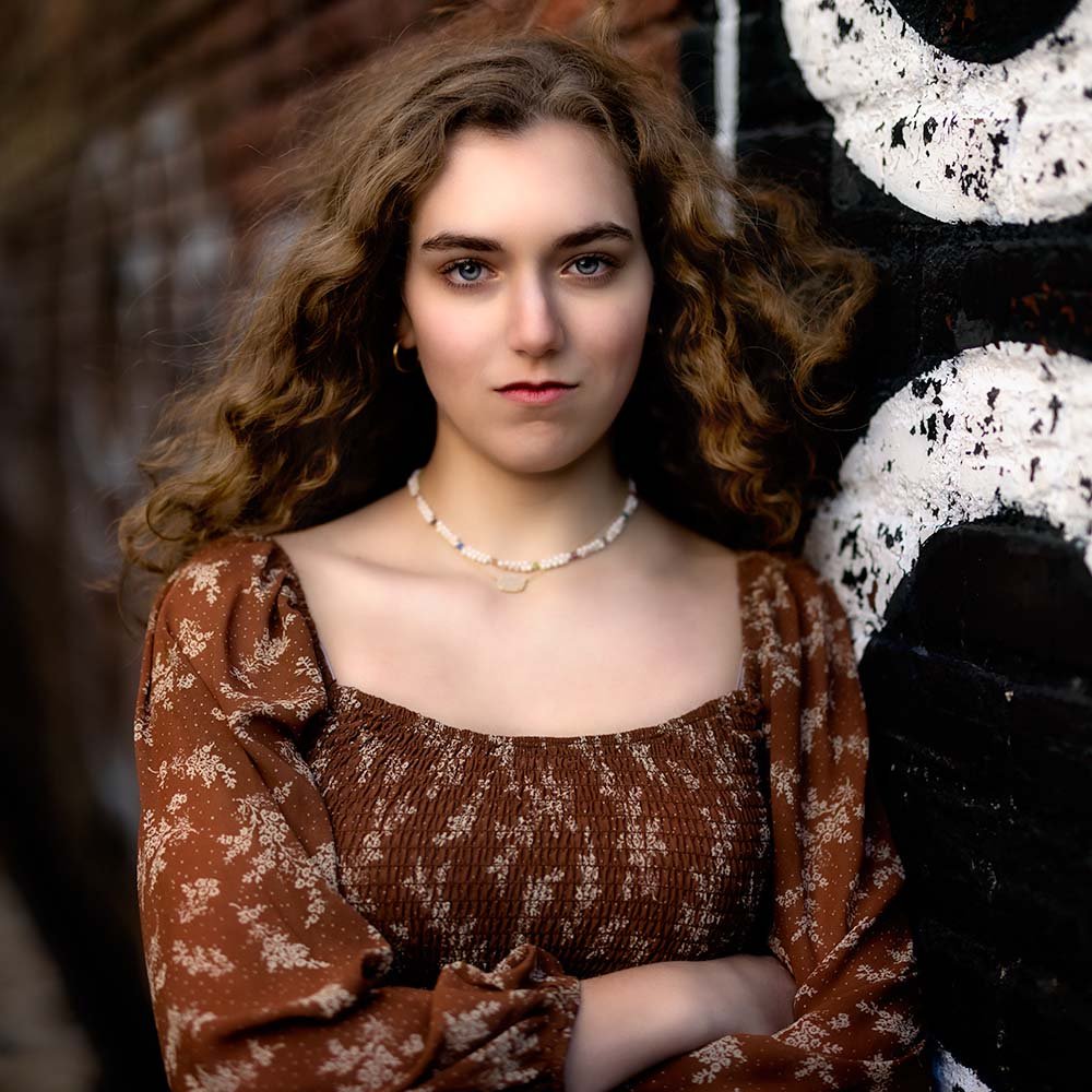 Don Evans Photography in Greensboro high school senior wearing a brown blouse leans on a wall while posing for her senior picture photo session